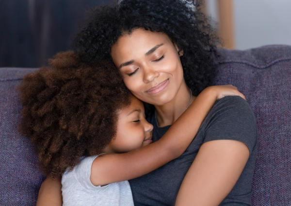 A young African American girl hugs her mother on the couch