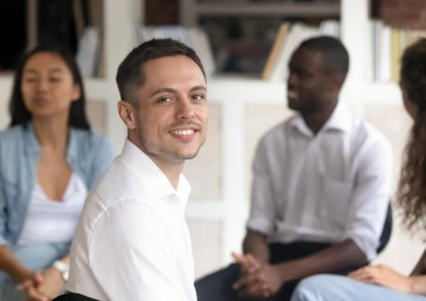 A man smiles while sitting in a circle during a group therapy session